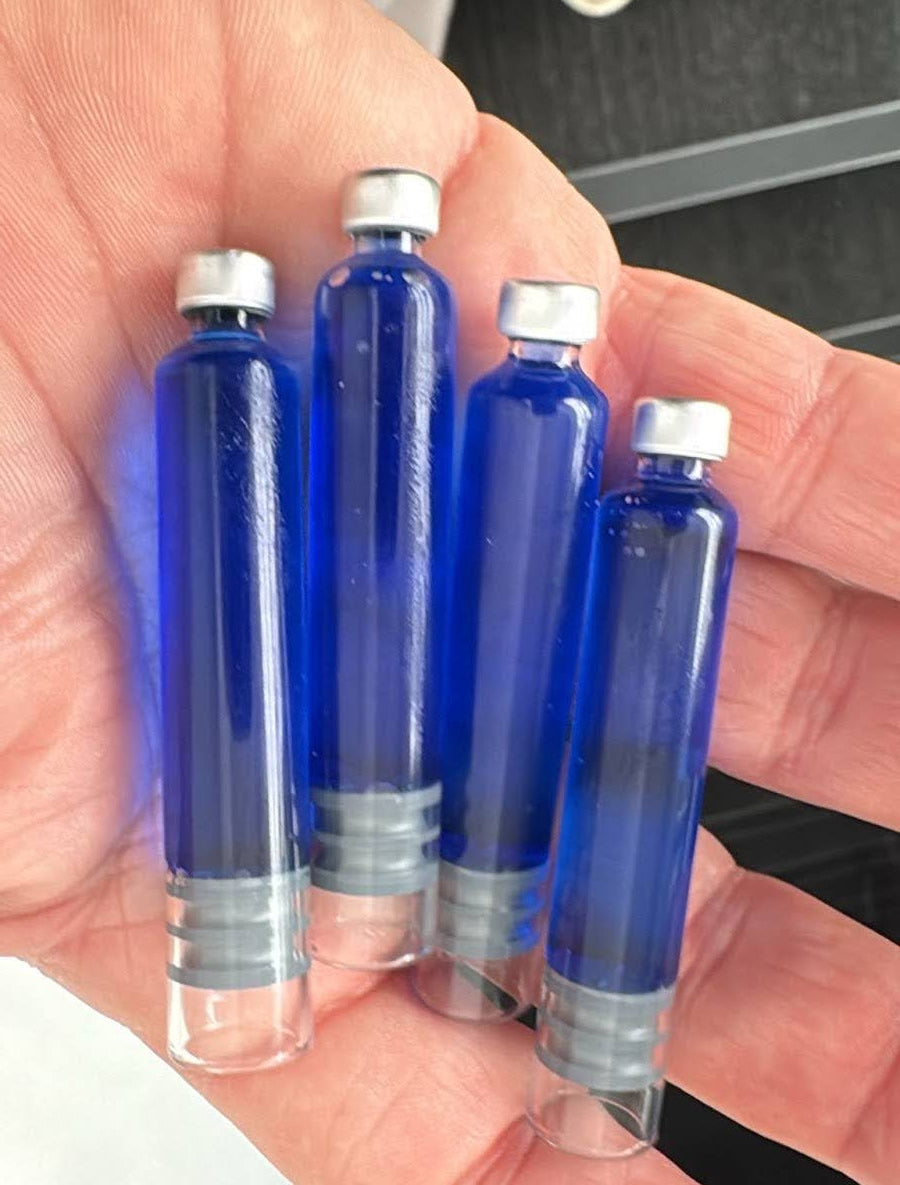 A hand holding four glass cartridges of bright blue GHK-Cu solution, visually representing the copper peptides researched for their ability to stimulate superoxide dismutase and boost antioxidant activity.